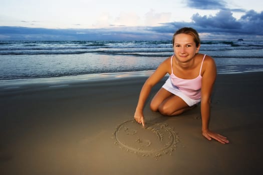 Young woman draws smile near the ocean on sunset time