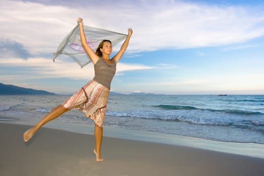Young woman dancing near the ocean on sunset time