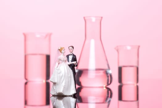 Chemistry of love concept. Wedding cake figurines and laboratory glassware against pink background.
