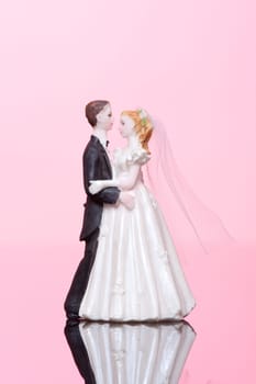 Wedding dancing figurines (bride and groom) on pink background.
