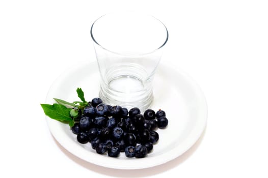 Blueberries and an empty juice glass on a white plate with a light colored background