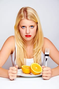Unhappy young woman eating fruit with cutlery