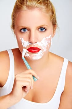 Young blonde woman with shaving cream shaving her face