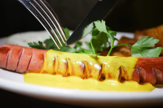 A person is preparing to eat a hot dog with mustard and garnish.