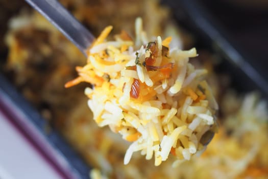 A colorful serving of biryani being lifted with a spoon during a meal.