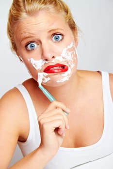 Young blonde woman with shaving cream shaving her face
