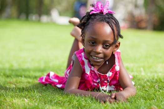 Outdoor portrait  of a cute little African american girl lying down on the grass