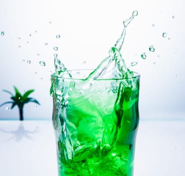 Splash of a green cocktail on a white background with a palm