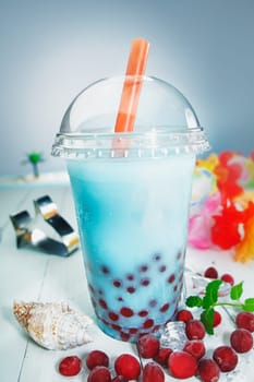 Colourful healthy boba or bubble tea with red berries served at the seaside on a tropical vacation