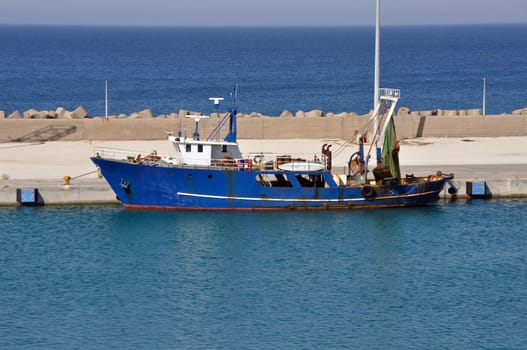 Fishing trawler in port. Rusty dragger ship tied to shore.