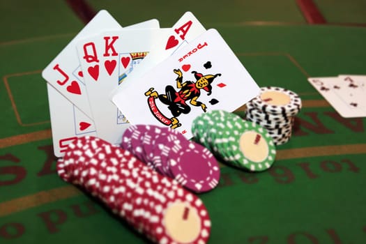 green casino table with chips and a hand of a royal flush in a poker game and a joker in the pack