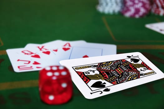 green casino table with dice and a hand of a royal flush in a poker game and the jack of spades in the pack