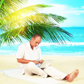Man with netbook working near the ocean under palmtree.