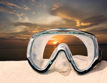 Diving equipment mask on white sand beach on sunset time.