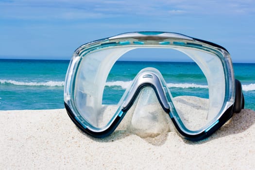 Diving equipment mask on white sand beach.