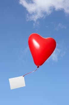 Red heart balloon with greeting card on ribbon against blue sky with clouds