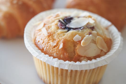 A fresh muffin garnished with almond slices sits on a plate.