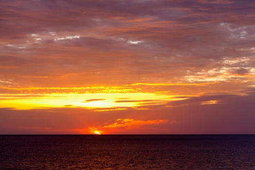 Image of the sun setting behind the ocean horizon with cloudy skies