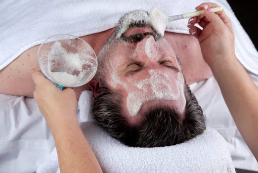 Hand of beautician applying cream to forehead of mature man having a facial.