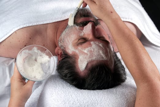 Hand of beautician applying cream to forehead of mature man having a facial.