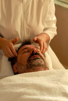 Hand of beautician applying cream to forehead of mature man having a facial.