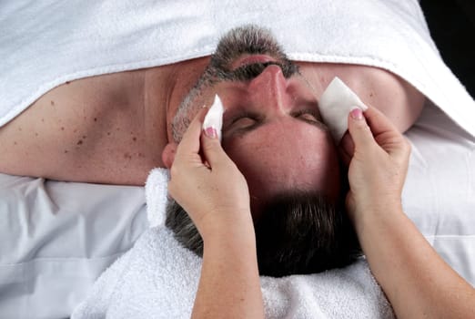 Hand of beautician applying cream to forehead of mature man having a facial.
