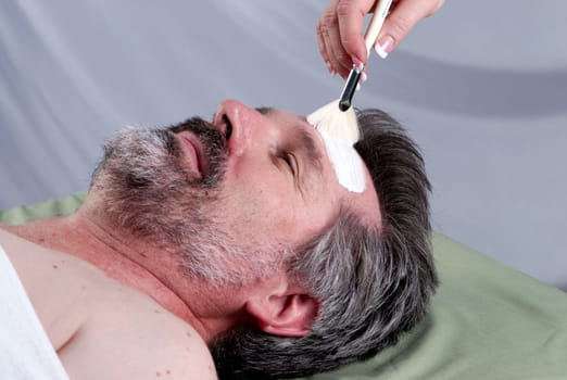 Hand of beautician applying cream to forehead of mature man having a facial.