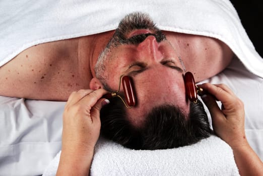 Hand of beautician applying cream to forehead of mature man having a facial.