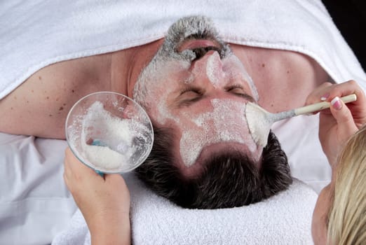 Hand of beautician applying cream to forehead of mature man having a facial.