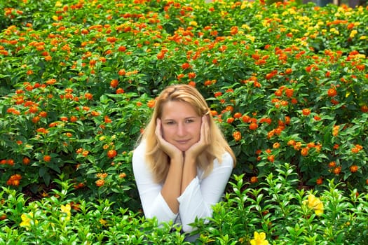 Young woman sitting in flowers. Face in her hands.