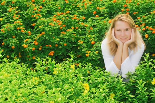 Young woman sitting in flowers. Face in her hands.