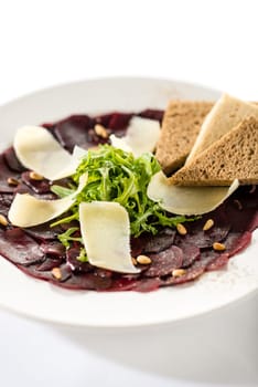 vegetarian carpaccio with beetroot, nuts and toast on white plate