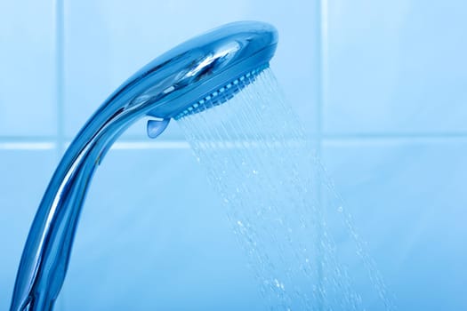 Shower head with water stream on blue background