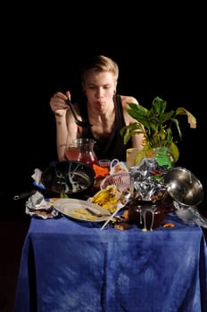 A young man with a spoon sits behind dirty table
