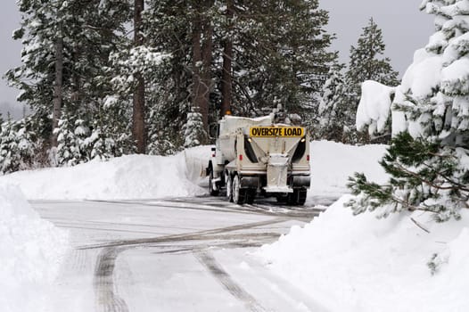 A large snow plow clearing a parking lot and road in the forest