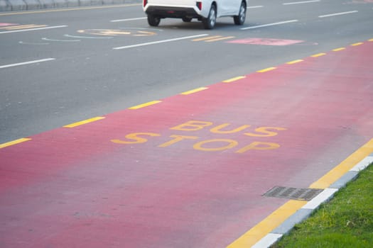 A bus stop is marked on a red lane along a busy road in daylight.