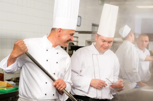 Two male cooks working in professional industrial kitchen prepare food
