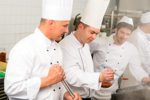 Two male cooks working in professional industrial kitchen prepare food