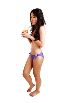 A very slim young Asian woman, with a glass of juice in her hand standing in her bikini and bare feet on white background.