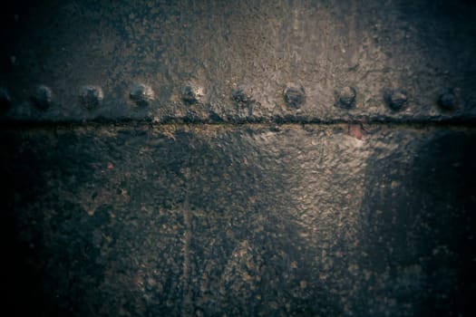 Pitted surface texture of old metal painted black with central highlight and riveted join