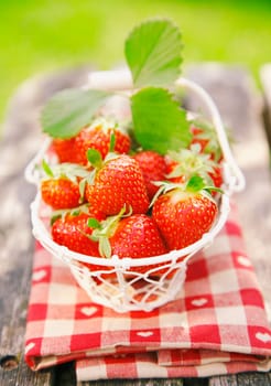 Fresh strawberries in small white basket on wooden table in nature - picnic meal