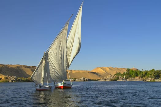 Typical sailing on the Nile. In the background sand hills and blue sky. (near Aswan, Egypt). Horizontally.