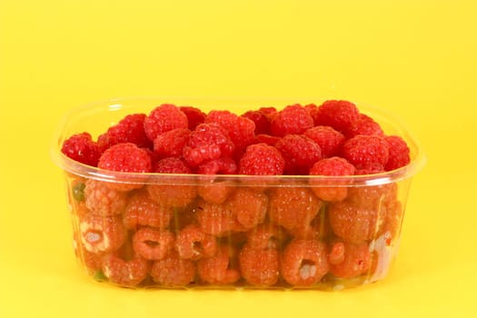 Fresh raspberries in plastic container on yelow background