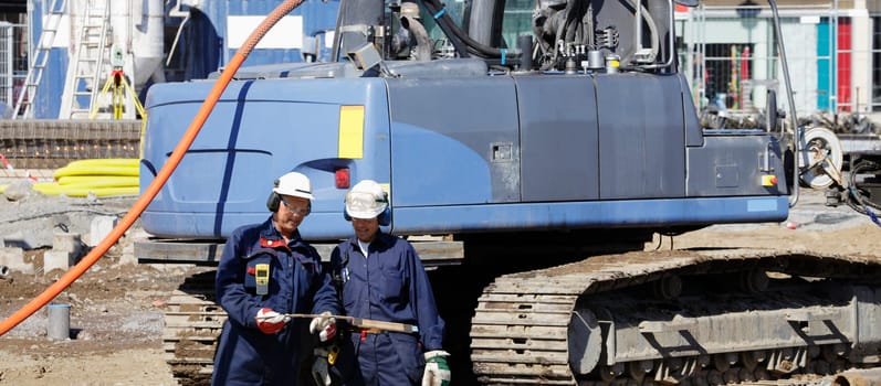 two building workers with giant heavy machinery in background