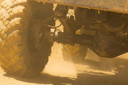 Detailed view of the wheels, tires and truck shaft that goes in the dust of the desert. The rays of light shine through the wheels.