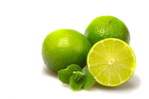 Two whole limes and one half lime with mint leaves. Isolated on white.