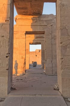 The interior of the Temple of Kom Ombo (near the Nile) in sunset light. On one of the pillars is a shadow of the Egyptian guide.