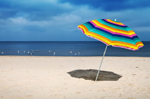 Colorful umbrella on a sandy beach, peaceful sea in a background