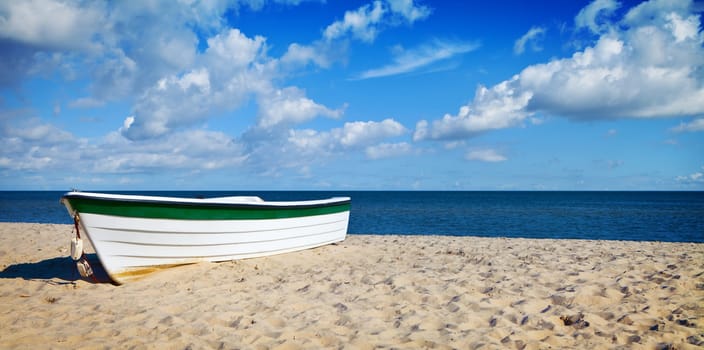 White boat on a sandy beach, blue sky with clouds, summertime