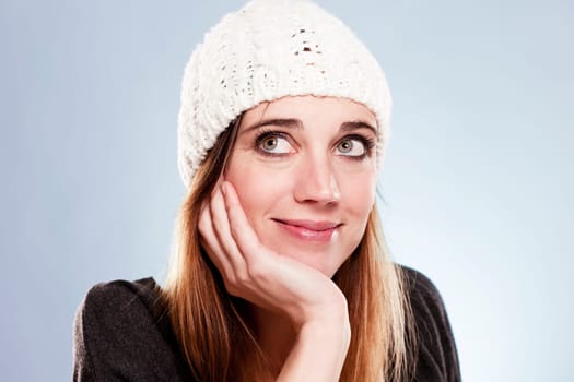 Smiling woman in winter cap looking up against bright blue background